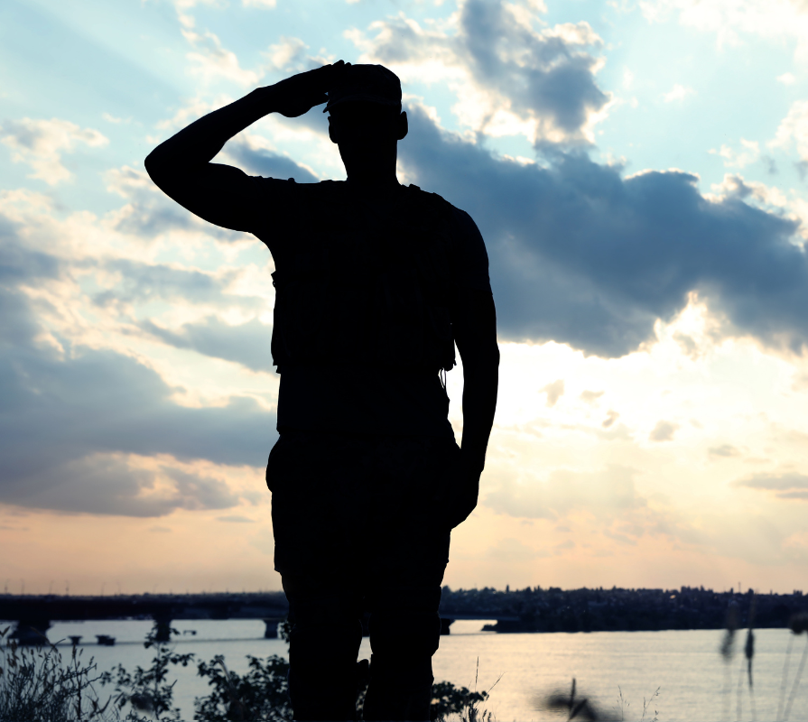 A silhouette of a man in uniform saluting with a dusky sky behind him.